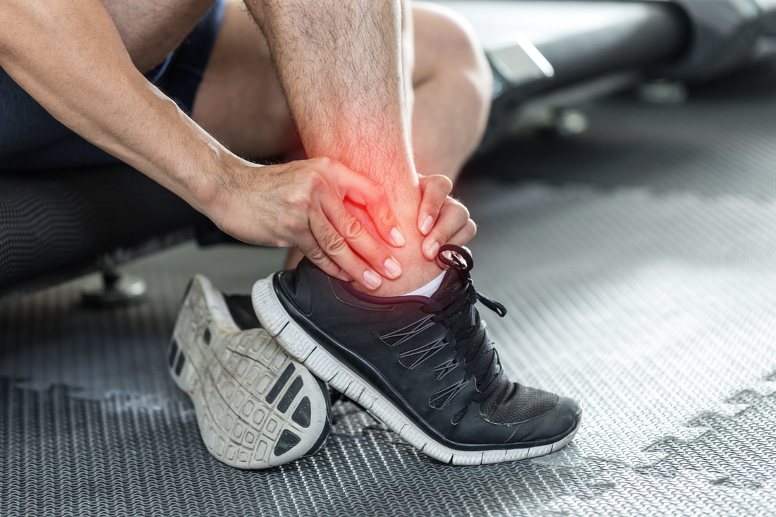 Person in running shoes holding a sore ankle, with the painful area highlighted in red